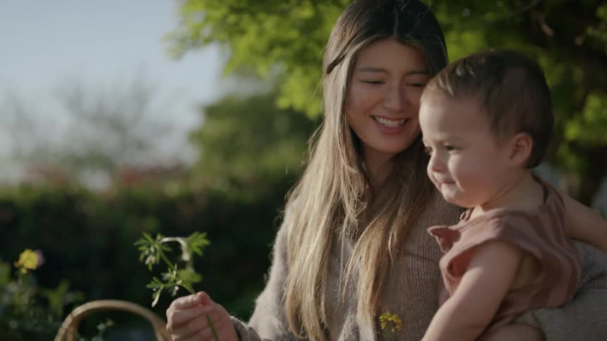 Mother with her daughter in an outdoor setting offering a leaf for her daughter to smell but the daughter doesnt like it