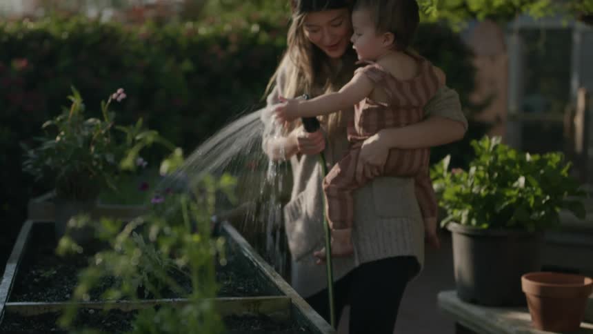 A mother wetting the vegetable plants while carrying her child