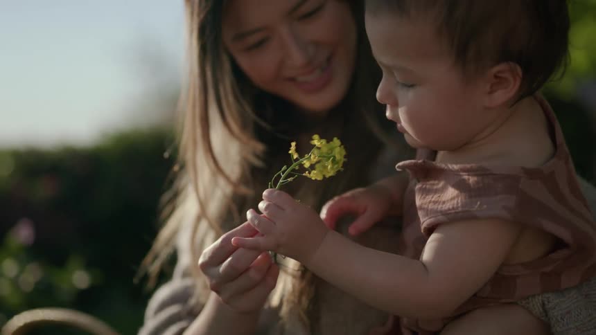 Mother gardening outdoors hands flower to child she is carrying