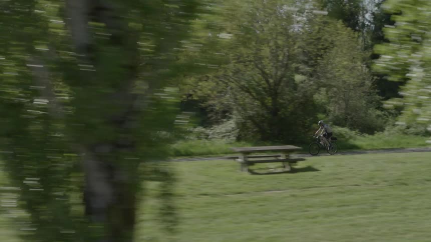 Bicycle rider on a paved bike path traveling through a park with grass and trees