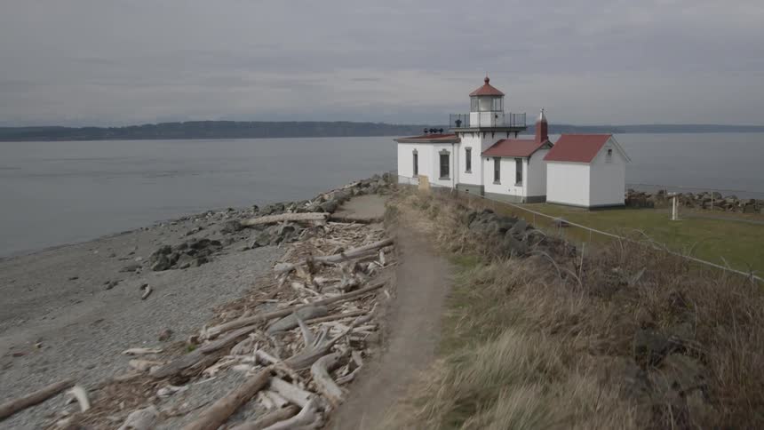 Flying above driftwood on a beach to reveal a lighthouse at the edge of the water