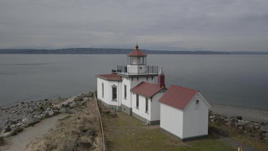 Flying over and past a red and white lighthouse next to the water