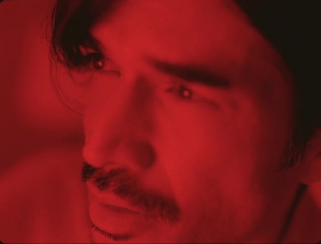 A man pokes his eye uncomfortably while a red light is illuminating his entire face