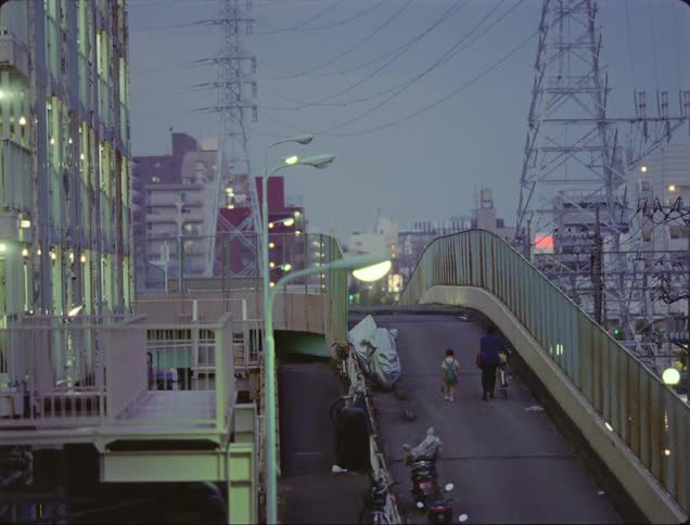 Man and a child walking with bicycle on a pedestrian bridge in a metropolis at dusk