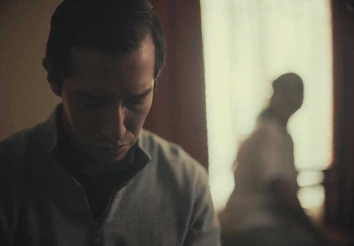 A man is standing still with worried expressions and behind him there is a woman with her back turned
