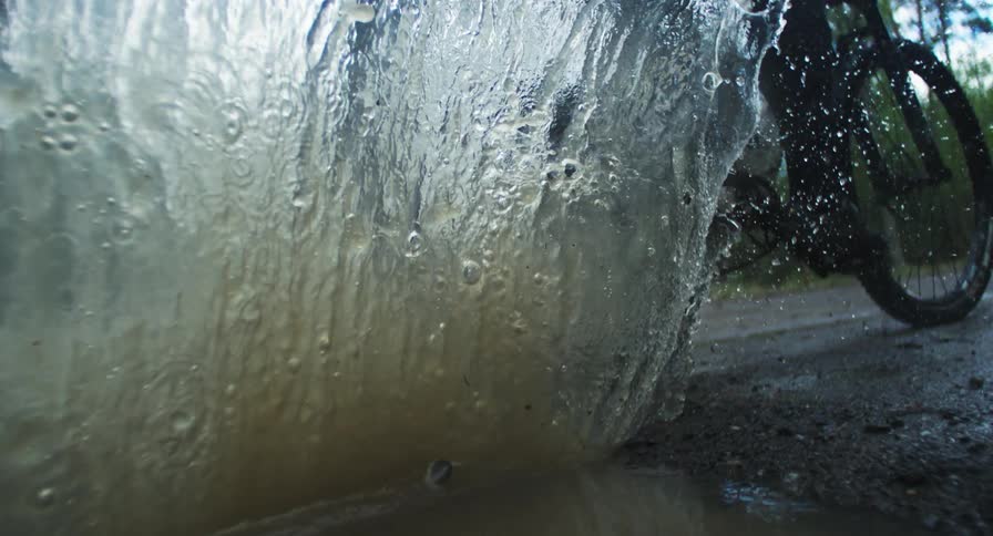 Person riding a bike through a puddle of water on a trail in nature