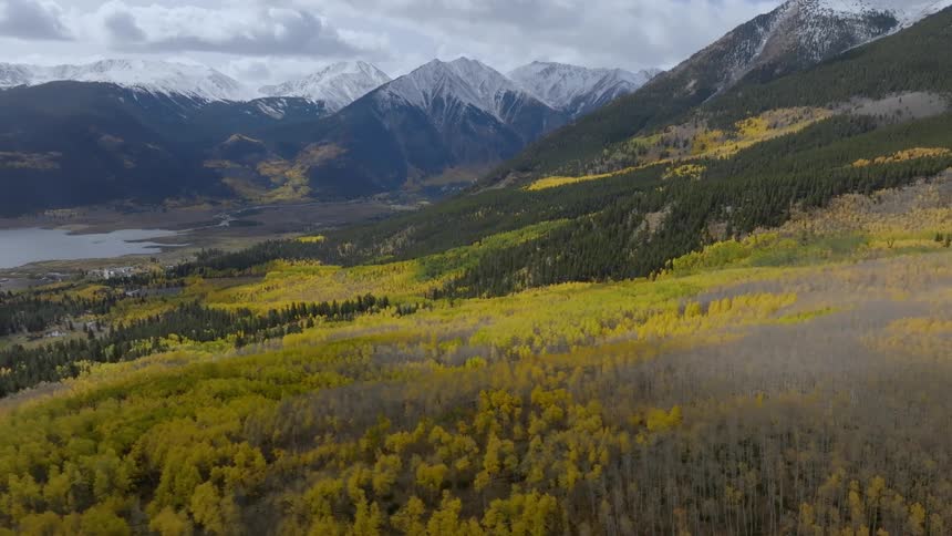 A landscape of a valley with goldenyellow foliage surrounded by mountains with snowy peaks under a cloudy sky