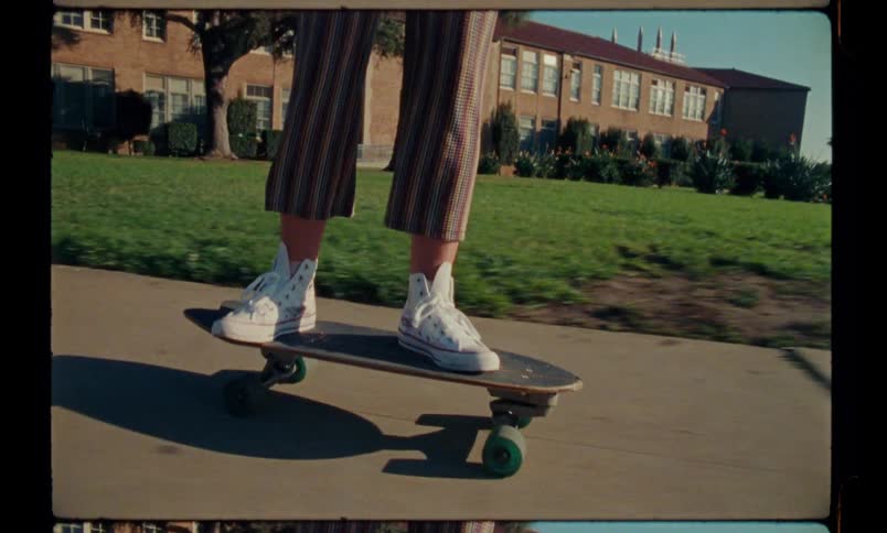 A teen skateboarding on the walkway in front of a brick building on a sunny day