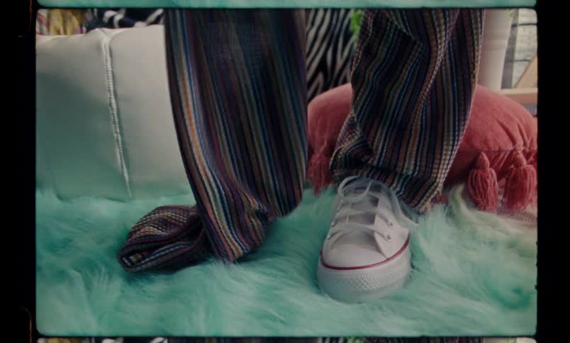 A person with white sneakers is standing on a blue plush rug and is wearing a dress