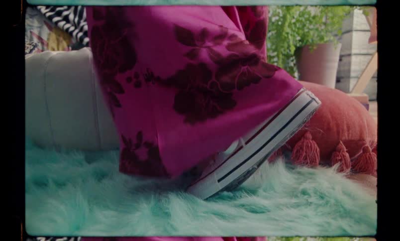 A person with white sneakers on a blue and furry rug is wearing a pink dress
