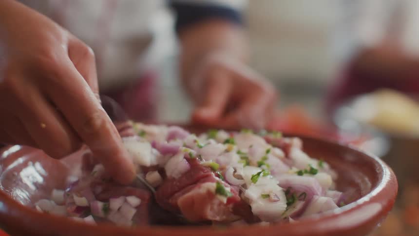 Closeup of a persons hands preparing a dish in a bowl with a spoon including proteins and vegetables