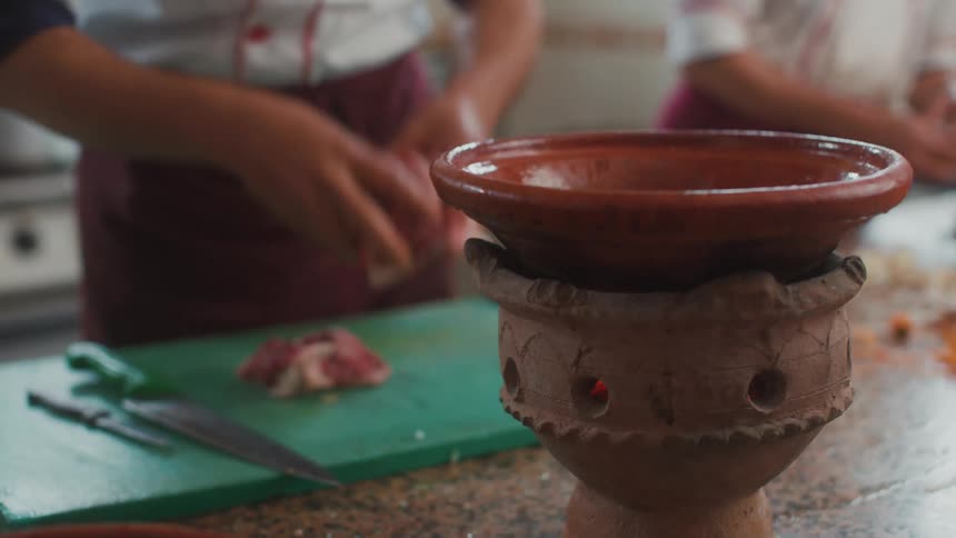 A chef cuts meat and puts the pieces in a bowl while another man peels onions in a restaurant