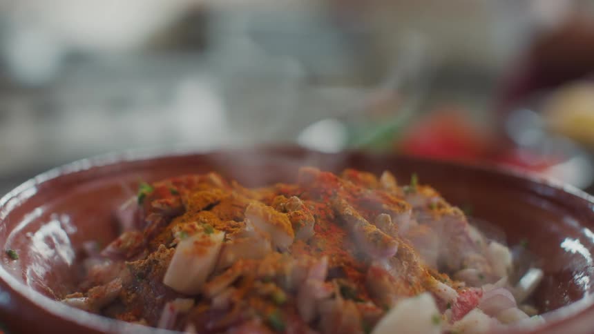 Hand of a person removing the lid and presenting a proteinrich and seasoned dish in a clay bowl