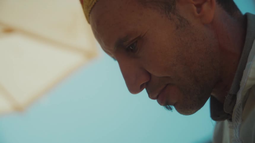 A man with facial hair and a hat is looking down