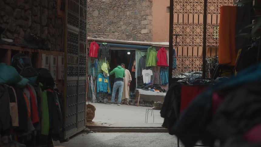 A clothing shop owner talks with a customer while a car drives by on the street