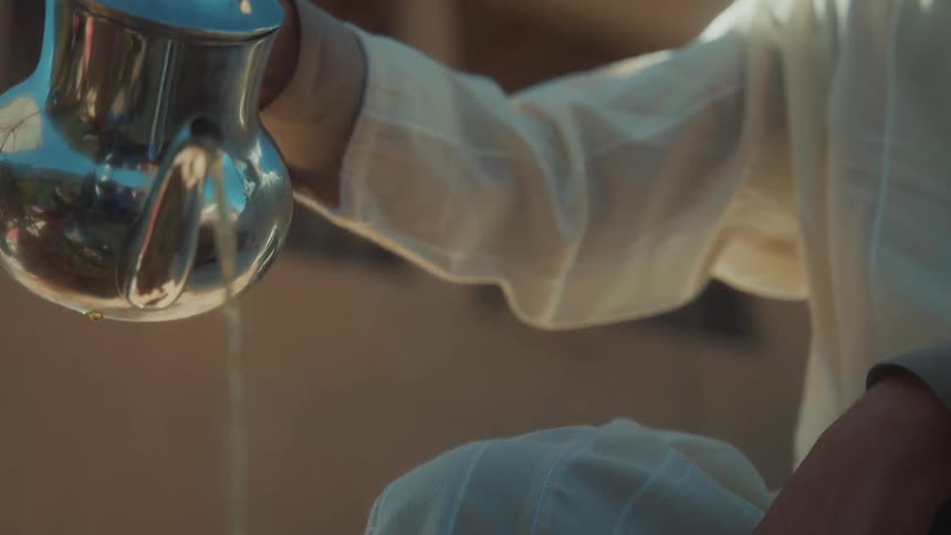 Man pours steaming water from metal pitcher while sitting outside