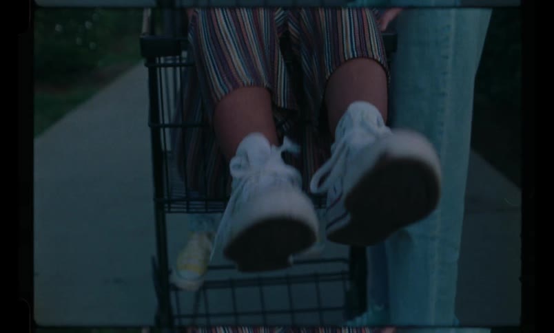 One person sits in a shopping cart while two others push and then ride it