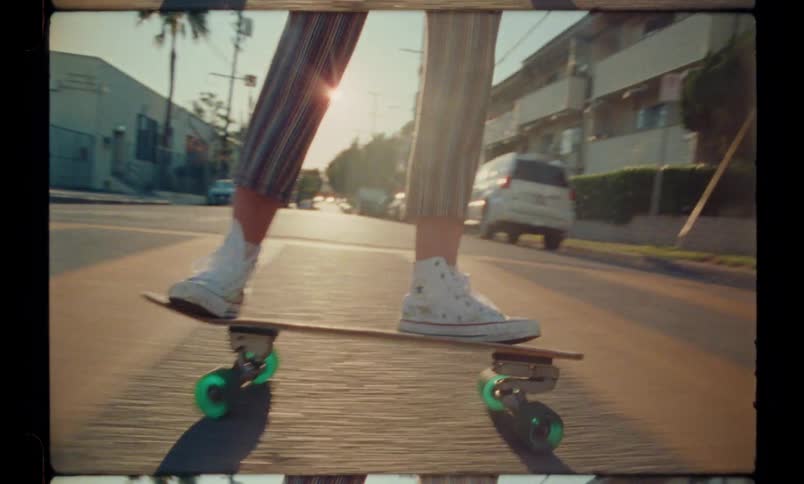 A woman wearing pants and white sneakers skateboards down the street during sunset