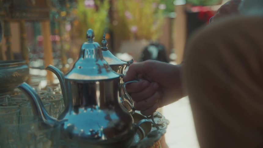 A human hand holding a reflective porcelain kettle