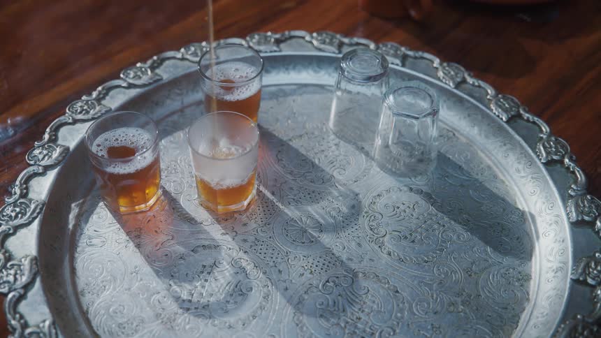 A person serves hot tea in small glasses over a metal tray