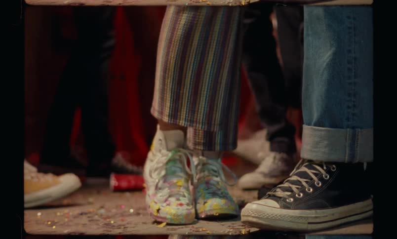 A woman wearing tennis shoes stands amidst many people at a party