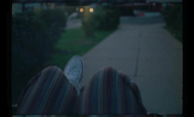 Legs of a person wearing white sneakers on a path that leads to a street with cars