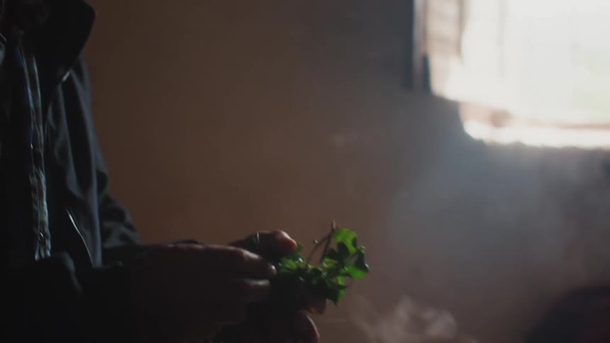 A man inside a room puts some herbs inside a smoky jug