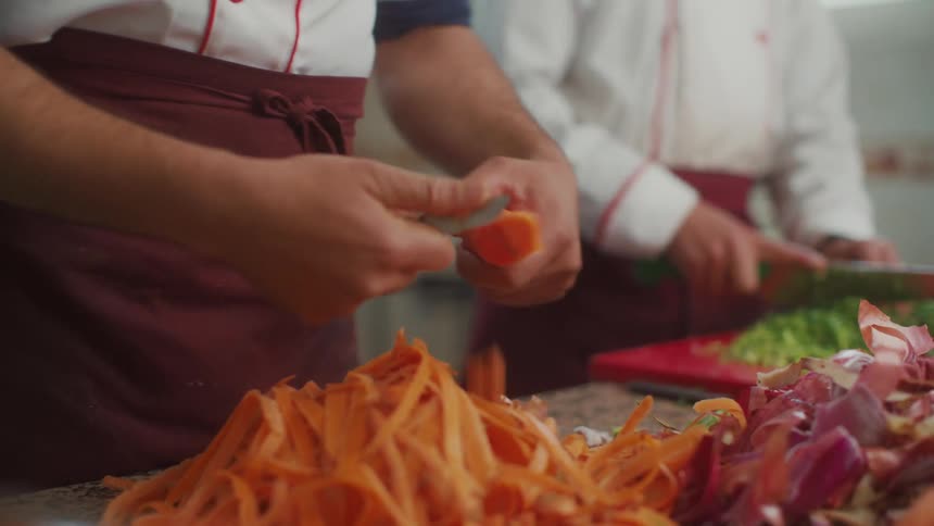 Two adults are peeling and chopping vegetables in a restaurant kitchen