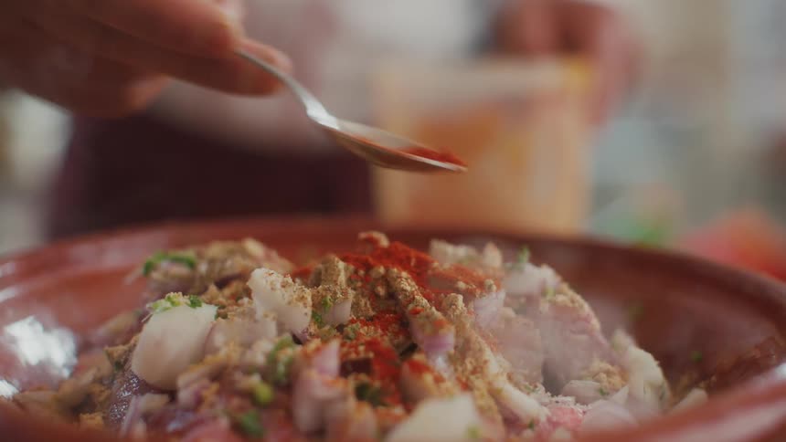 Cook adds spice onto meat dish steaming in clay dish