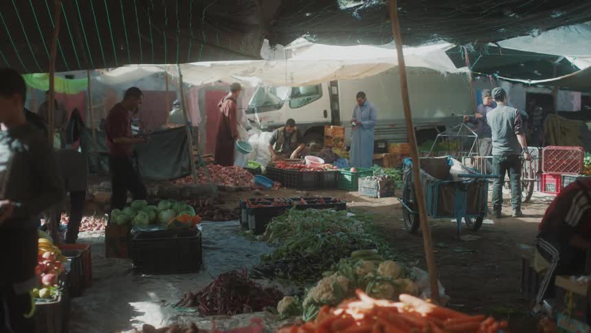 View of people working with vegetables in crates and on the ground in a grocery market under tents