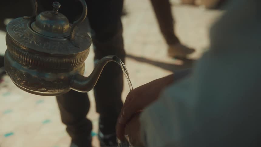 A man pouring water from a teapot into another mans hands