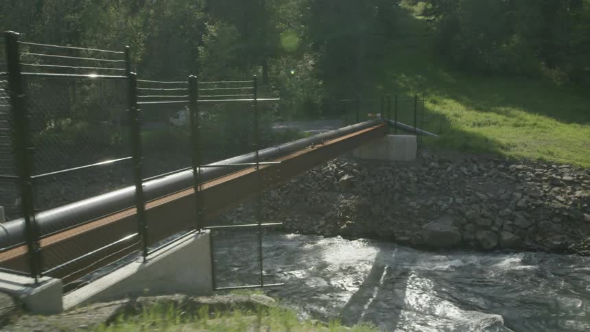 Following a safety inspector approaching a fuel pipeline that crosses over a fast flowing river