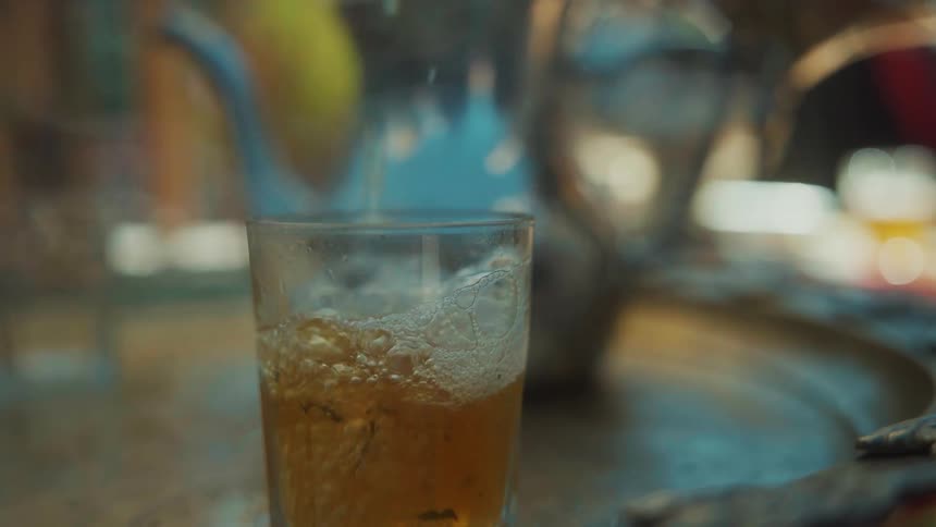 An adult pours hot tea from a teapot into a clear drinking glass
