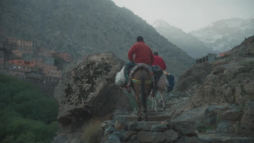 Two people riding pack animals in a region with mountains of rocks