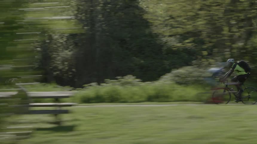 A bicycle messenger races down a trail as trees wipe through the foreground