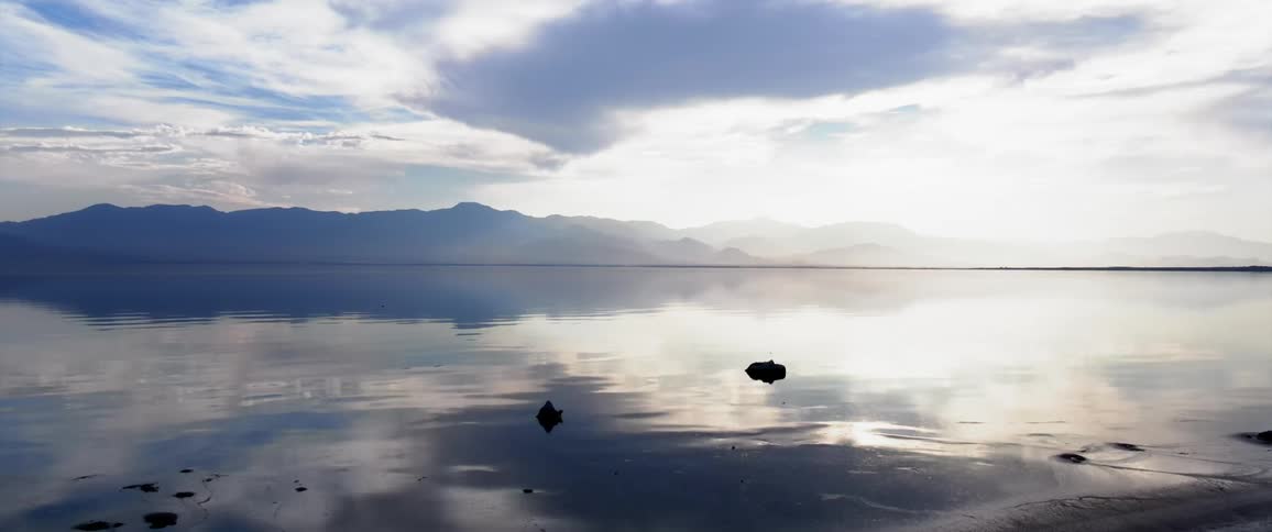 Landscape facing a calm sea with a mountain range on the horizon under a morning sky