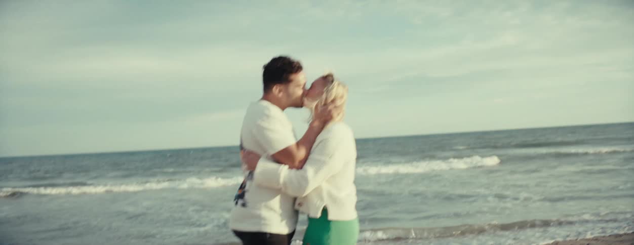 A man and a woman are kissing in front of a beach