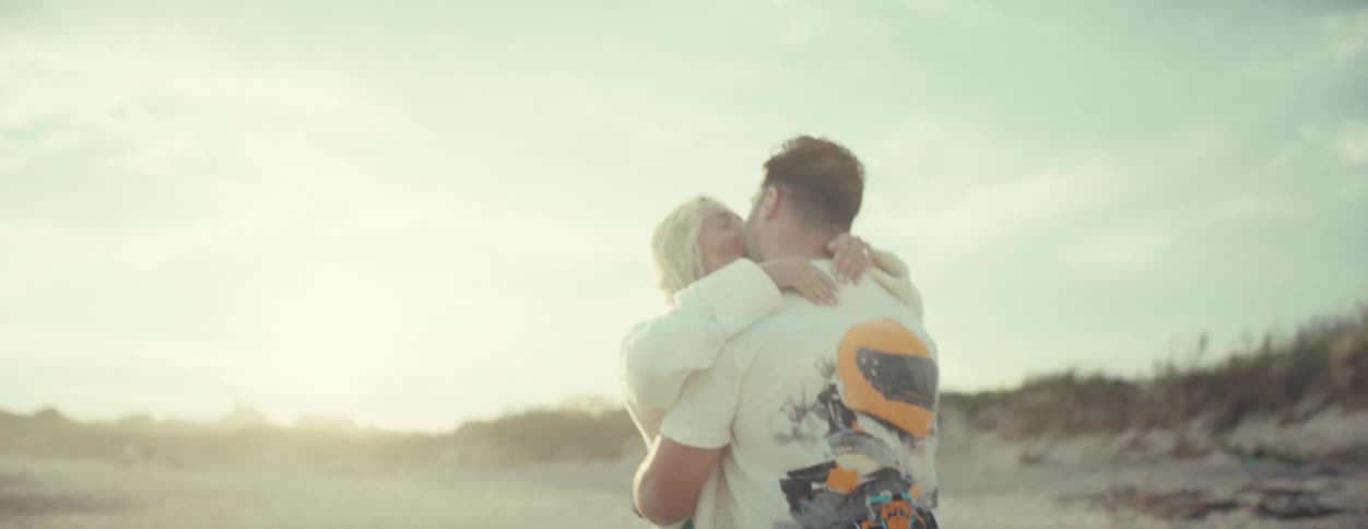 Couple stands on beach kissing on a sunny day