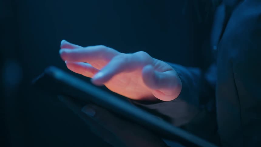 Hands of a woman operating a tablet in a dark room