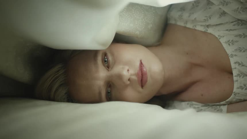 Light fades on woman lying on her side under bed covers