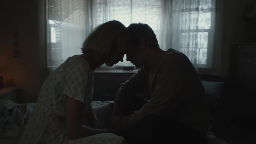 Man and woman locked their foreheads together while seated on the bed indoor at midday