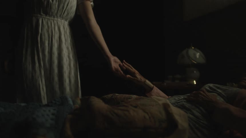 View of an elderly person lying down holding hands with a woman who is standing
