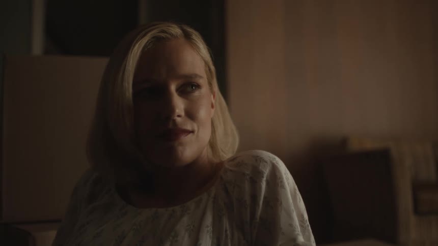Blonde woman wearing a white dress listens to man smiling in the living room