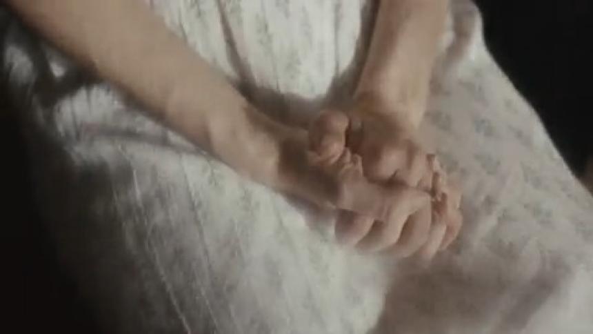 Close up of a woman with a white dress sitting in chair and clasping hands together