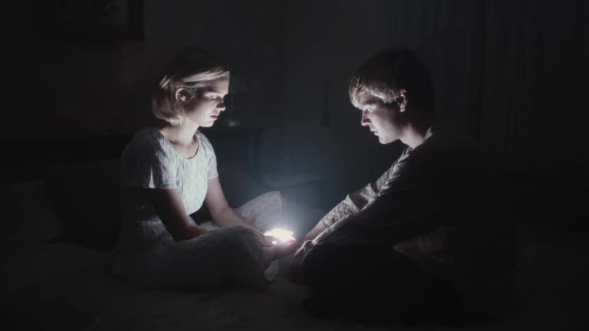 A male and a female sitting on the bed in the dark and starring at the bright light