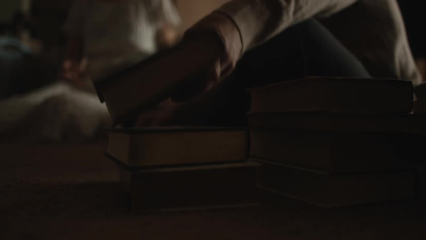 A person arranging books in a pile on the floor