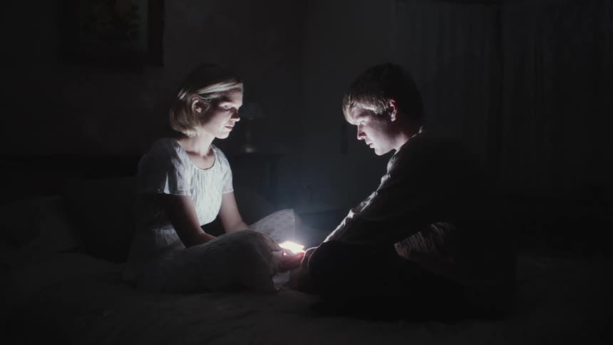 A male and female sitting on the bed starring at the bright light