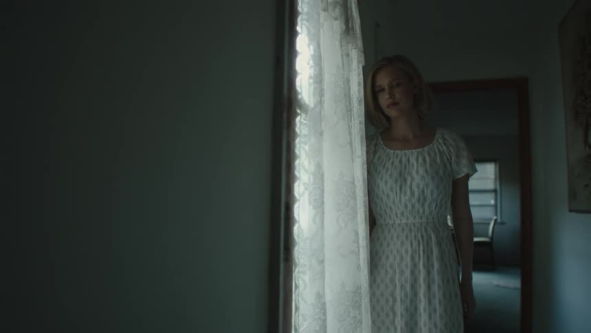 Woman in a white dress looking pensively out a window