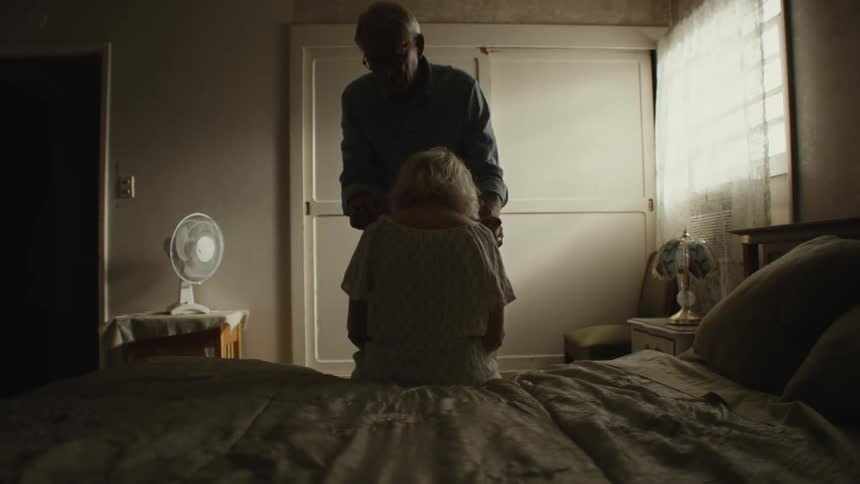 Elderly man helps old woman dress in the bedroom