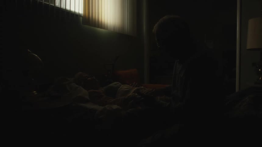 An elderly man sitting beside a child laying on a bed as he comfort him with the time going between night and day fast